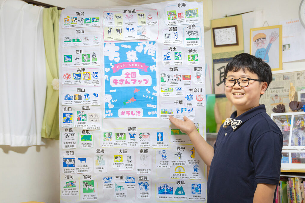 大坂聡志さん。全国各地の牛乳パックに描かれた牛のイラストを調べてまとめた自作の「全国牛さんマップ」ととともに。